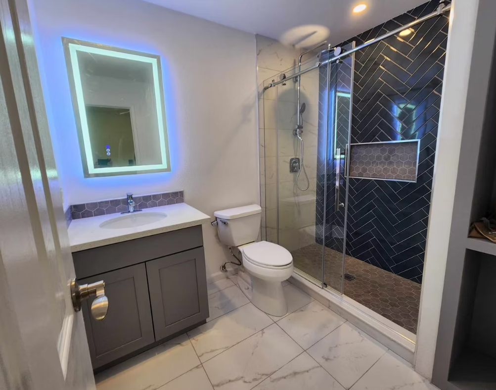 Walk-in shower with black herringbone tile and LED-backlit mirror, installed for a Redmond homeowner